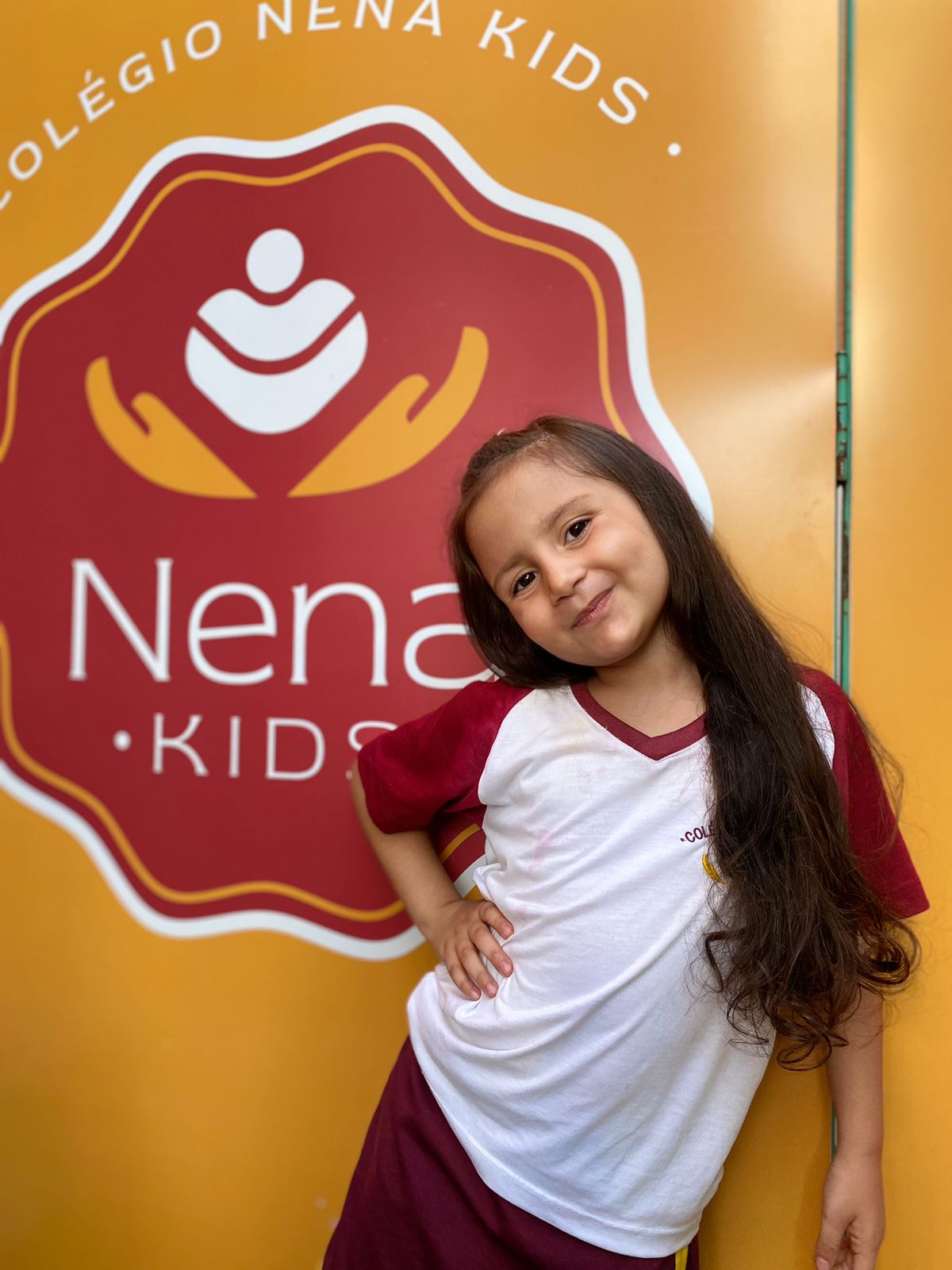 Aluna do Colégio Nena Kids em frente à marca da escola